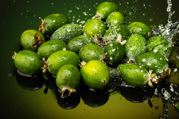 several feijoa fruits with drops and splashes of water on dark glass with gradient background and reflection