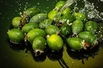 several feijoa fruits with drops and splashes of water on dark glass with gradient background and reflection