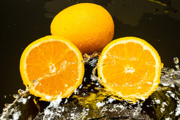Fototapeta na wymiar two oranges, whole and cut in half with drops and splashes of water on dark glass with gradient background and reflection