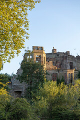 Fototapeta premium An eerie abandoned English Manor House, with overgrown forest trees and foliage surrounding the building and broken brickwork, depicting a scary halloween haunting atmosphere with ravens on the roof