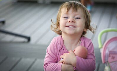 Cute Adorable 18 Month Old Baby Girl with Big Blue Eyes and Brown Curly Hair playing with Doll. Happy healthy kid play alone on the Porch.