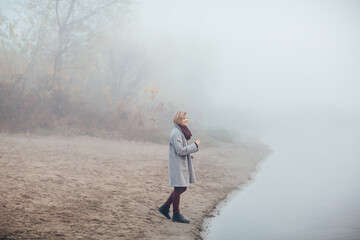 A girl runs along the shore of the lake in a foggy morning. She is having fun and has a good mood