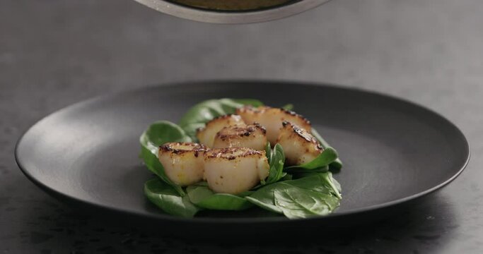 Slow motion drizzle roasted scallops on spinach with juice from frying in black plate