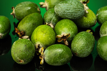 several feijoa fruits scattered on dark glass with gradient background