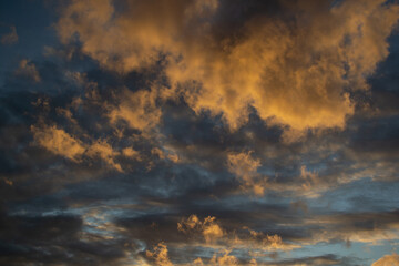 Sunset evening blue sky with fluffy airy orange yellow clouds in light of sun against a background of dark clouds of different shapes