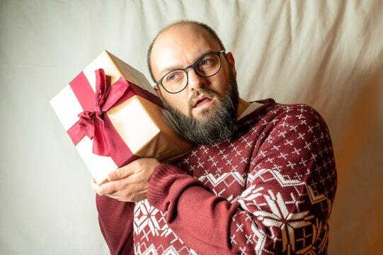 man carefully holds a present to his ear to find out what is inside