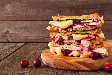 Grilled holiday turkey, cranberry and brie sandwiches. Side view stack on a serving board against a...