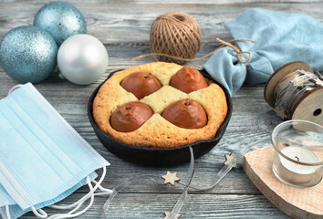Christmas table with protective masks, cake, and Christmas decorations on a wooden background. Side view. The concept of celebrating Christmas during the coronavirus.