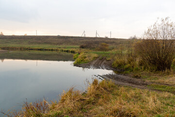 Obraz premium autumn rural natural landscape with calm river water reflecting yellow trees and dry grass in cloudy day