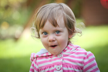 Close Up Portrait of a little 18 Month Old Girl with  Big Blue Eyes and Curly Hair, a girl Playing Outside, Funny Face Expression, Happy baby