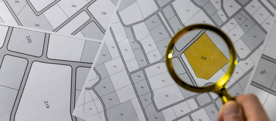 hand with magnifier on cadastre map - search and buy land concept. banner copy space - obrazy, fototapety, plakaty