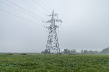 Close up view of electric power line towers align on farming field meadow. Hazy weather on flatland with low visibility. Wide angle