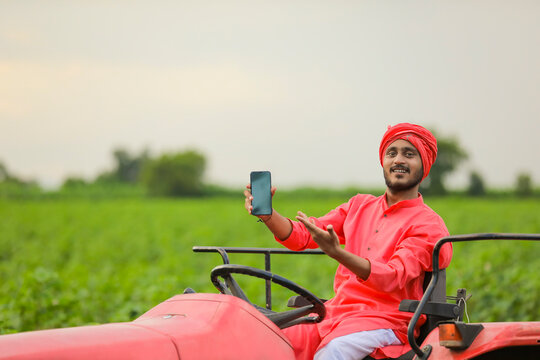 Young Indian Farmer Showing Smartphone Or Tablet On Tractor