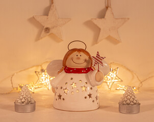 christmas festive scenery showing an angel ornament in warm golden light; front view with blurred bokeh star lights background on white wooden table