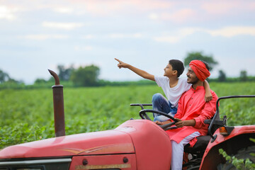 Indian farmer and cute little child enjoying tractor ride in agriculture field