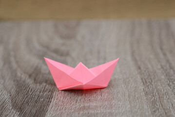 Pink origami boat on wooden background