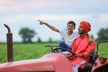 Naklejka premium Indian farmer and cute little child enjoying tractor ride in agriculture field