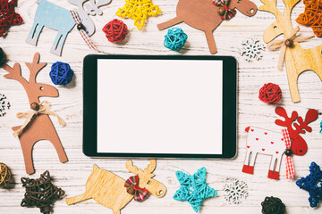 Top view of tablet on holiday wooden background. New Year decorations and toys. Christmas concept