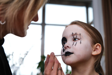 Mother is helping caucasuan daughter with Halloween makeup indoor