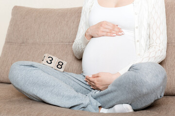 Pregnant woman in white underwear on bed in home holding calendar with weeks 38 of pregnant. Maternity concept. Expecting an upcoming baby
