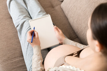 Pregnant woman makes notes. Concept of pregnancy, health care, medicine. Mother waiting of baby at the home