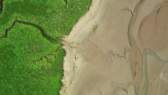 Aerial top down view of the coast line at low tide, showing the natural pattens in the golden sand and green grass.