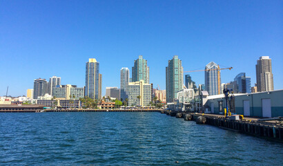 Fototapeta na wymiar San Diego city buildings, showing the skyscrapers of downtown rising above harbour viewed from sea. Clear sky without clouds and tall buildings.