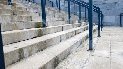 External multi-stage stone staircase. There are a lot of stairs and railings made of metal. Many steps in an urban environment, symbolic abstract background.