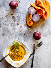 Traditional pumpkin soup with freshly baked seeds and onions served on a white stone base.