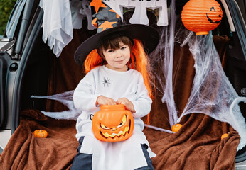 Trick or trunk. Trunk or treat. Little child in witch hat celebrating Halloween party in decorated...
