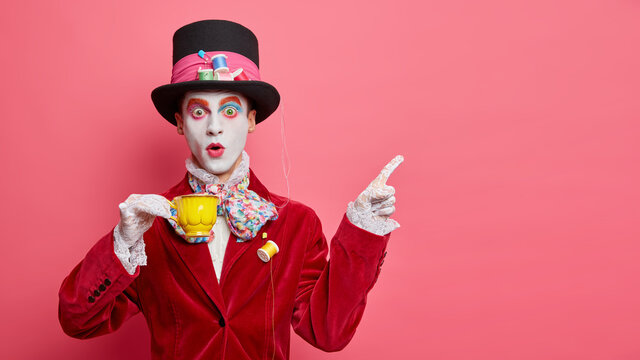 Insane mysterious unique character obsessed with tea drinking dressed fashionably has big hat points at upper right corner against pink background. Mad hatter demonstrates direction on empty space