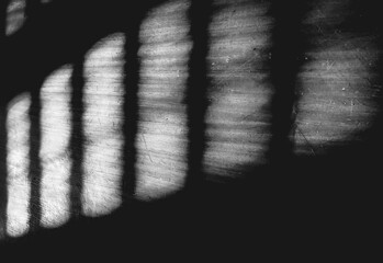 Shadow from the blinds, abstract background. Bright sunlight shines through the blinds and leaves shadows on the wall or floor,  black and white image.