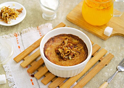 Kugelis, baked potato pudding made from grated raw potatoes in a white portioned baking dish on a concrete gray background.