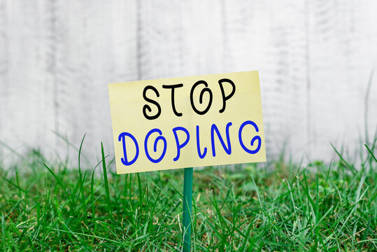 Word writing text Stop Doping. Business photo showcasing quit the use of banned athletic performanceenhancing drugs Plain empty paper attached to a stick and placed in the green grassy land