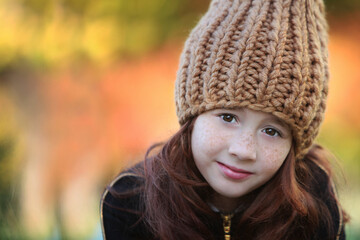 A girl in a warm knitted hat on the background of an autumn forest. Bokeh effect in the background. Headpiece for the cold season.