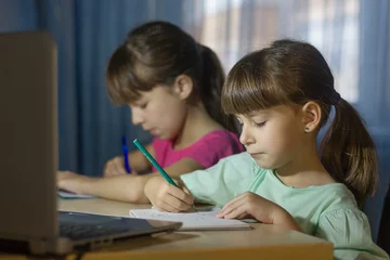 Deurstickers Online onderwijs op afstand. Twee schoolmeisjes studeren thuis en schrijven huiswerk © Albert Ziganshin