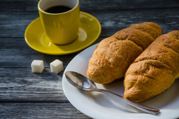 Still life with cup of coffee and croissant on the wooden background. Old retro camera and postcard are near the cup.