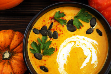 Roasted pumpkin and carrot soup with cream and pumpkin seeds on wooden background.