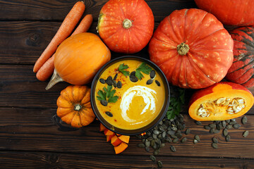 Roasted pumpkin and carrot soup with cream and pumpkin seeds on wooden background.