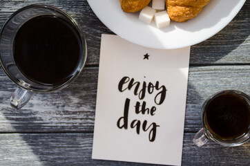 Still life with cup of coffee and croissant on the wooden background. Old retro camera and postcard are near the cup.