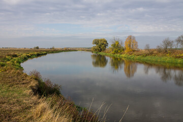 Autumn landscape - bend of the river with yellow grass and reflection of the cloudy sky and space for copying