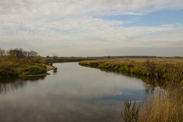 Autumn landscape - bend of the river with yellow grass and reflection of the cloudy sky and space for copying