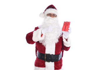 Senior man wearing a traditional Santa Claus costume holding a small red paper wrapped gift in one hand and pointing at it with the other.  Isolated on white.