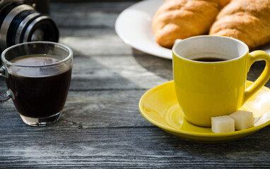 Still life with cup of coffee and croissant on the wooden background. Old retro camera and postcard are near the cup.
