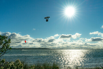 A kite boarder flips above the water while silhouetted in front of the sun.