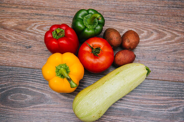 Red tomatoes and colored bell peppers on a dark wooden background. Raw vegetables. Green zucchini with new potatoes.