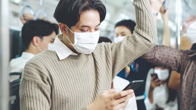 Traveler Wearing Face Mask While Using Mobile Phone On Public Train . Coronavirus Disease Or COVID 19 Pandemic Outbreak And Urban City Lifestyle Problem In Rush Hour Commuting Concept .