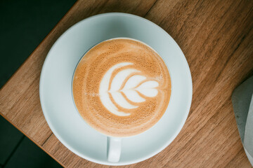 Beautiful cup of cappuccino with latte art in space wooden background. Fashionable toning. Minimal composition, hipster vibration. Top view, flat copy space for text.