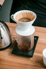 Dripping coffee with his hand, Barista pours water on ground coffee with a filter. Coffee shop worker standing at the counter with hand drip coffee set.