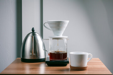 Homemade drip coffee using glass jug, metal filter and grinder with beans on wooden table over white background.